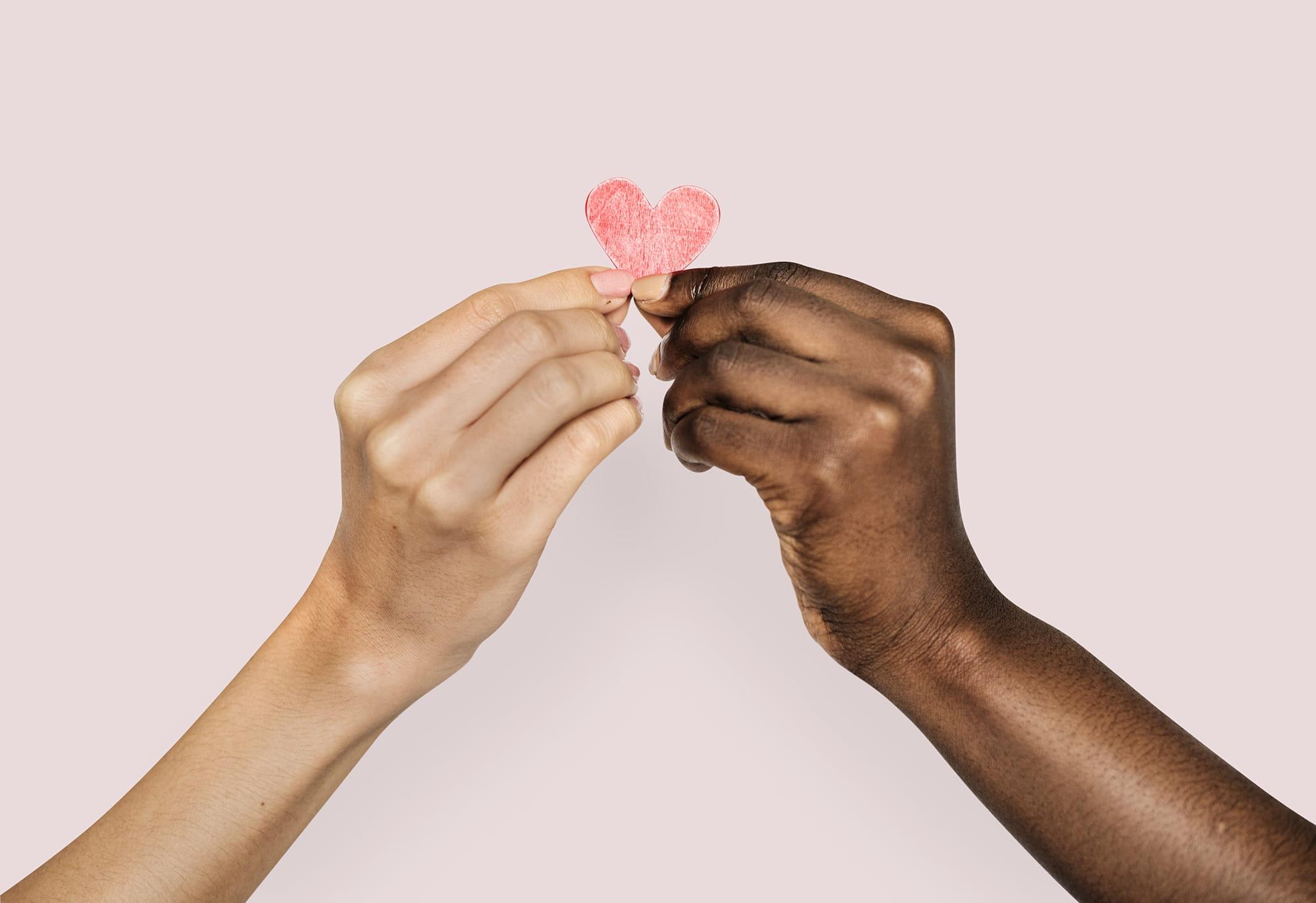 Two hands of different people holding a paper heart