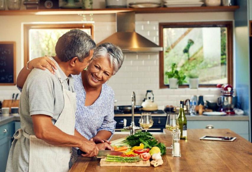 Older couple smiling, cutting vegetables together in kitchen