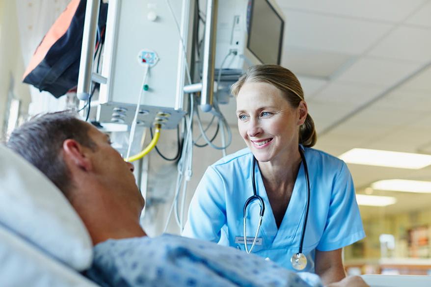 Healthcare professional smiles while caring for patient in hospital bed